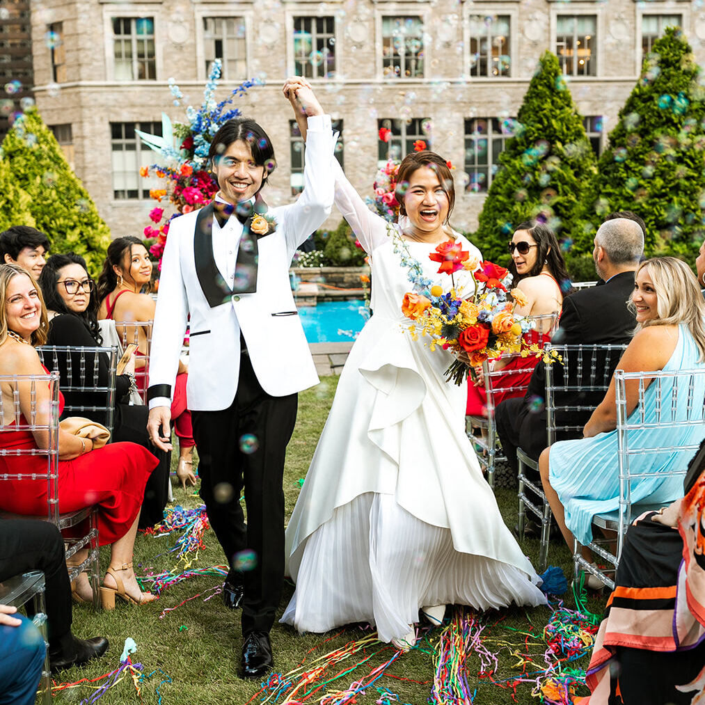Best Places for a Colorful Wedding: A bride and groom smiling hand in hand, walking down a grassy rooftop aisle at 620 Loft & Garden.