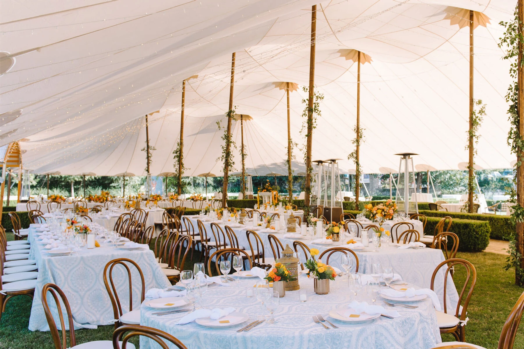A tented reception at an Indian fusion wedding featured blue-and-white table linens, citrus-hued centerpieces, and poles wrapped with greenery.